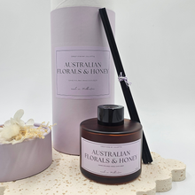 Load image into Gallery viewer, Luxury reed diffuser home fragrance in 100ml amber glass bottle with black reeds. Presented in lilac cylinder box ready for gifting. Fragrance Australian Florals & Honey.