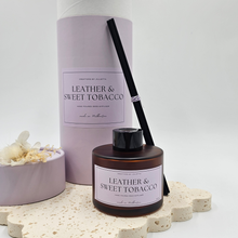 Load image into Gallery viewer, Luxury reed diffuser home fragrance in 100ml amber glass bottle with black reeds. Presented in lilac cylinder box ready for gifting. Fragrance Leather and sweet tobacco.