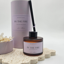Load image into Gallery viewer, Luxury reed diffuser home fragrance in 100ml amber glass bottle with black reeds.  Presented in lilac cylinder box ready for gifting. Fragrance By the fire
