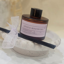 Load image into Gallery viewer, A bottle of Japanese Honeysuckle with diffuser sticks on a textured surface.
